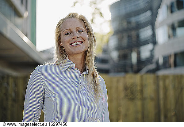 Lächelnde blonde Unternehmerin in Geschäftskleidung im Finanzviertel