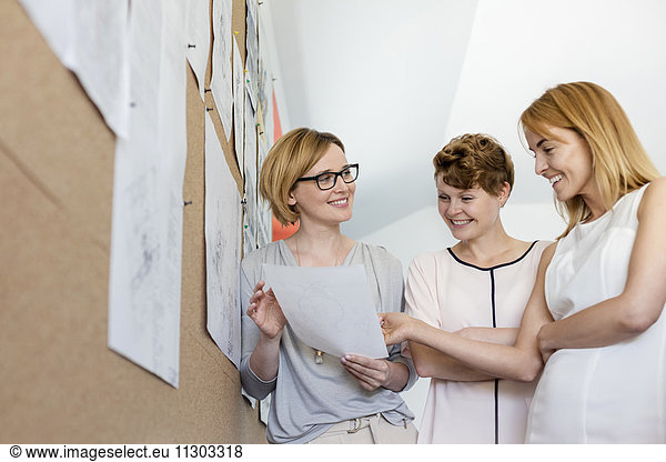 Lächelnde Designerinnen beim Prüfen von Proofs am Schwarzen Brett im Büro