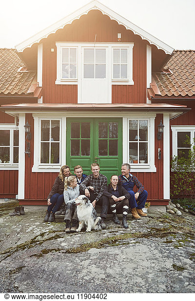 Lächelnde Familie sitzend mit Haustier am Hauseingang