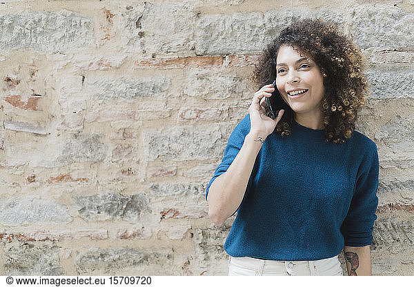Lächelnde Frau am Telefon an einer Steinmauer