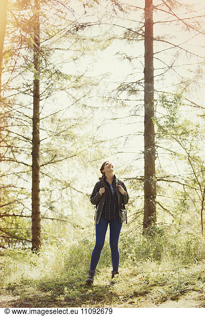Lächelnde Frau beim Wandern mit Blick auf sonnige Bäume im Wald