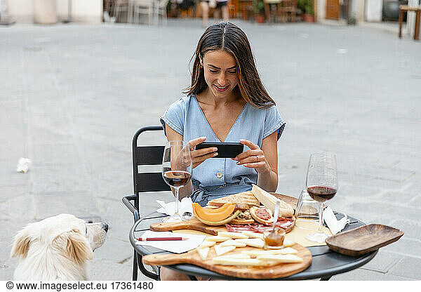 Lächelnde Frau fotografiert Essen und Trinken in einem Straßencafé