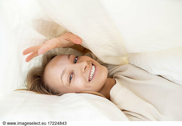 Lächelnde Frau in Decke auf Kissen liegend