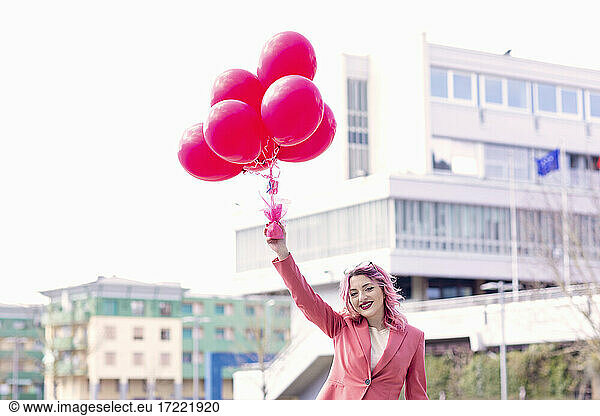 Lächelnde Frau in Freizeitkleidung hält Heliumballons