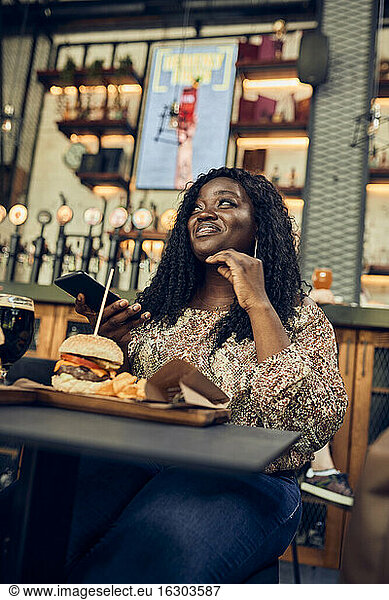 Lächelnde Frau isst einen Burger in einer Kneipe