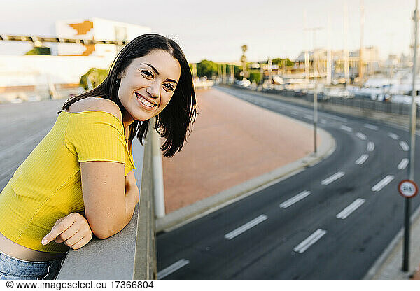 Lächelnde Frau lehnt an einem Brückengeländer