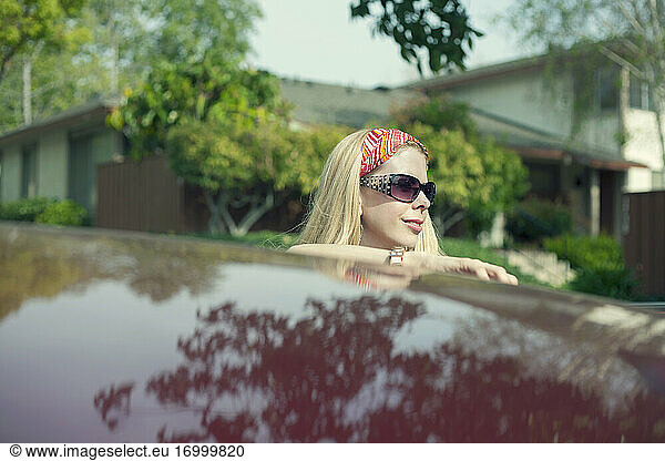Lächelnde Frau lehnt sich auf dem Autodach bei einem Road Trip an einem sonnigen Tag