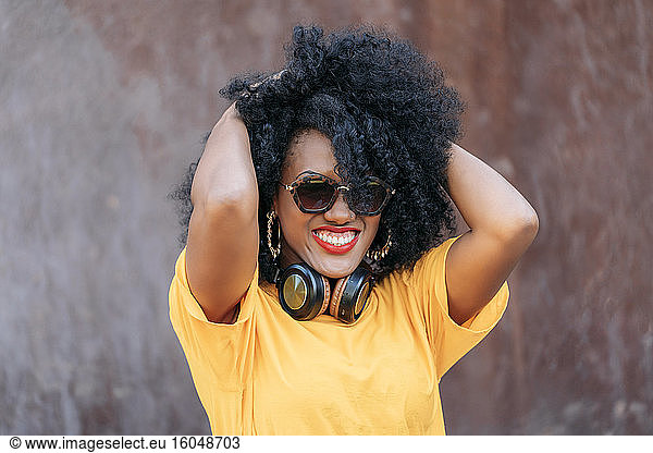 Lächelnde Frau mit Afro-Haar und Sonnenbrille und Händen im Haar