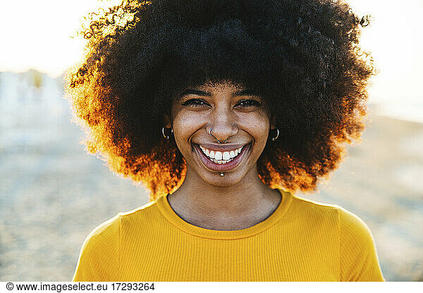 Lächelnde Frau mit Afrofrisur am Strand bei Sonnenuntergang