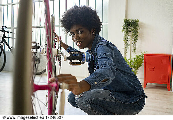 Lächelnde Frau mit Afrofrisur repariert Fahrrad zu Hause