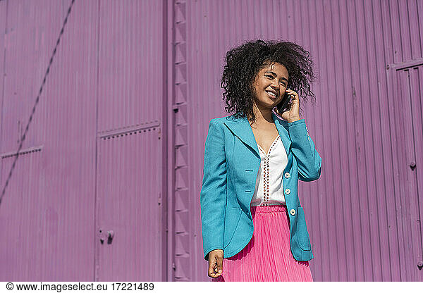 Lächelnde Frau mit Afrofrisur telefoniert an einem sonnigen Tag