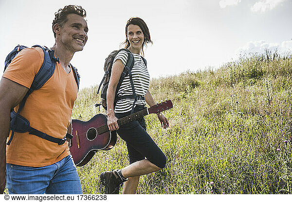 Lächelnde Frau mit Gitarre geht an einem Mann im Gras vorbei