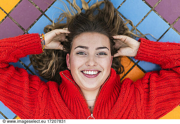 Lächelnde Frau mit Hand im Haar auf Fliesenboden liegend