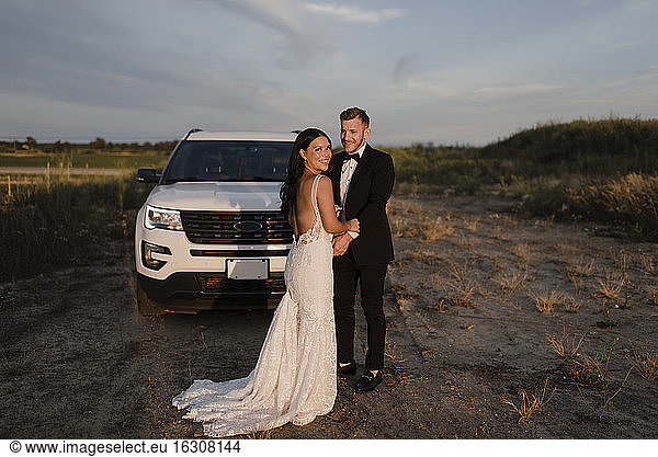 Lächelnde Frau mit männlichem Partner vor einem Auto auf einem Feld stehend
