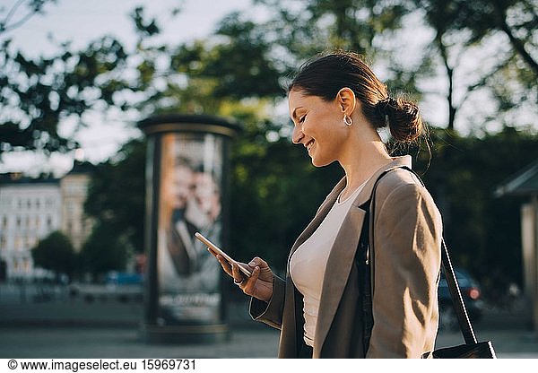 Lächelnde Frau nutzt soziale Medien  während sie in der Stadt steht