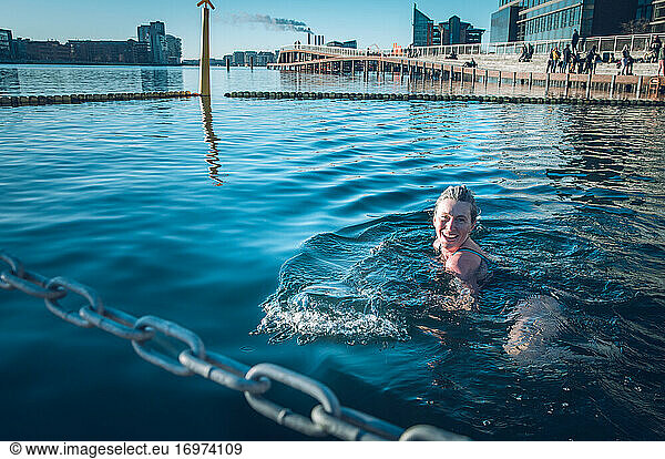 Lächelnde Frau schaut in die Kamera und schwimmt in kaltem Wasser in Dänemark