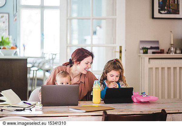 Lächelnde Frau sieht Mädchen an  die während des Essens einen Film auf einer digitalen Tablette sehen