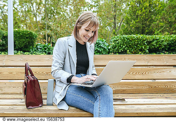 Lächelnde Frau sitzt auf Parkbank mit Laptop