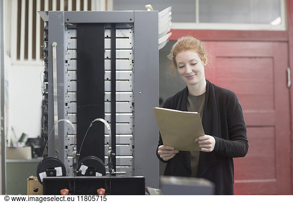 Lächelnde Frau steht an einer Druckmaschine und hält ein Dokument