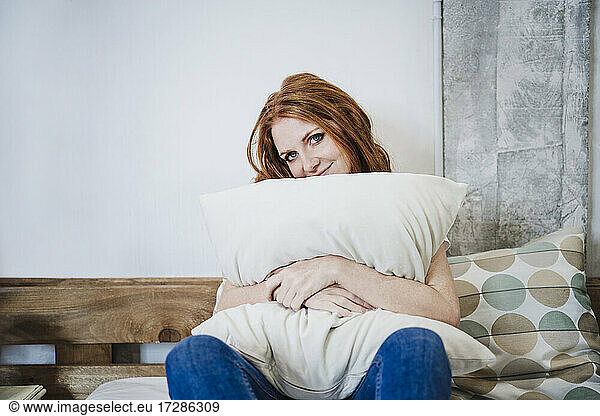 Lächelnde Frau umarmt Kissen zu Hause