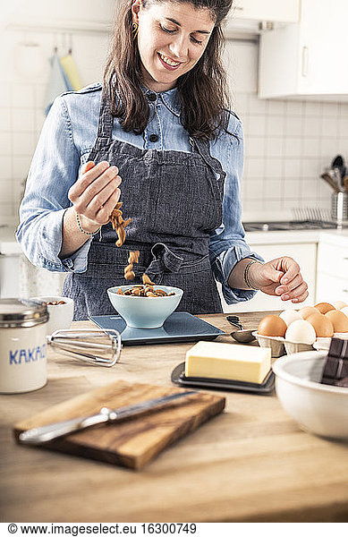 Lächelnde Frau wiegt Mandeln auf einer Küchenwaage zu Hause