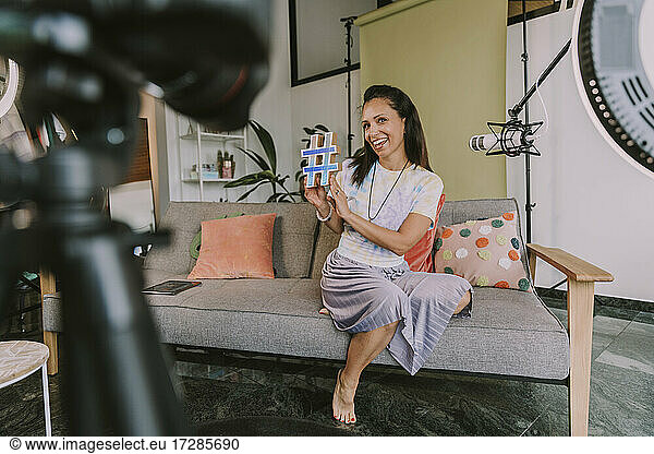 Lächelnde Frau zeigt Hashtag-Symbol beim Vloggen zu Hause