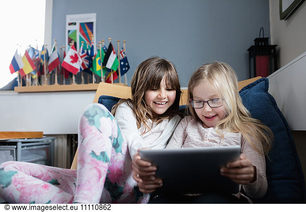 Lächelnde Freunde  die in der Schule auf dem Sofa liegen und ein digitales Tablett benutzen.