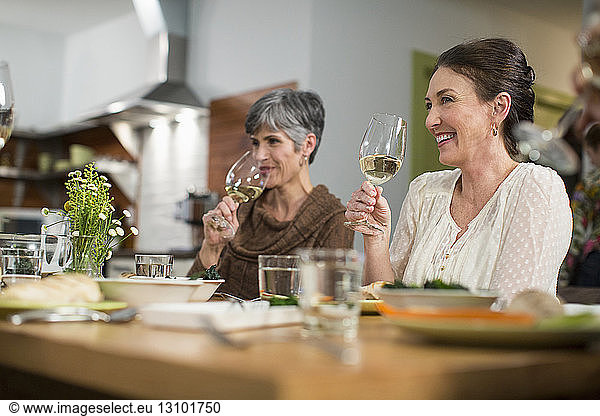Lächelnde Freundinnen  die Wein trinken  während sie bei geselligem Beisammensein am Tisch sitzen