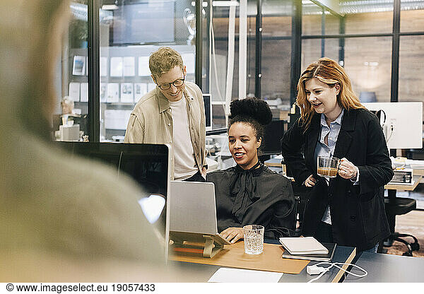 Lächelnde  gemischtrassige Kollegen  die über einem Laptop diskutieren  während sie eine Strategie im Büro planen