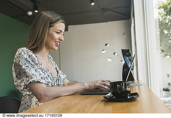 Lächelnde Geschäftsfrau arbeitet an einem Laptop auf einem Tisch in einem Café
