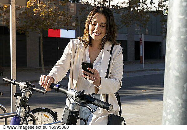 Lächelnde Geschäftsfrau beim kontaktlosen Bezahlen an einer Fahrradparkstation