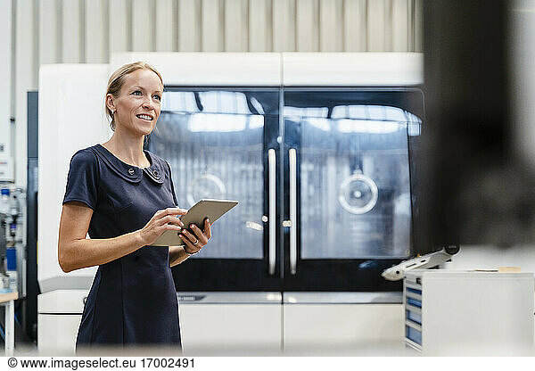 Lächelnde Geschäftsfrau  die ein digitales Tablet hält  während sie in einer Fabrik steht