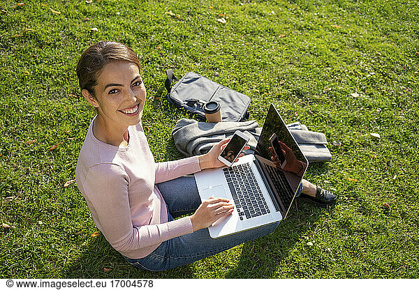 Lächelnde Geschäftsfrau  die im Herbst im Park im Gras sitzt