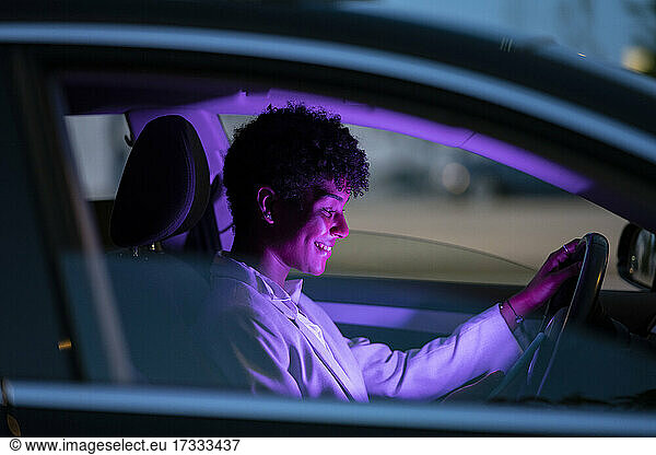 Lächelnde Geschäftsfrau in beleuchtetem lila Auto bei Nacht