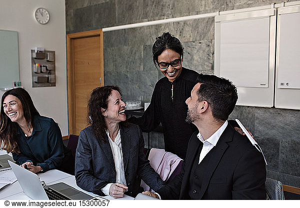 Lächelnde Geschäftsfrau interagiert mit fröhlichen Kollegen im Büro