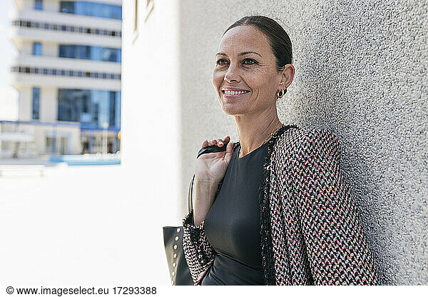 Lächelnde Geschäftsfrau mit Handtasche an die Wand gelehnt