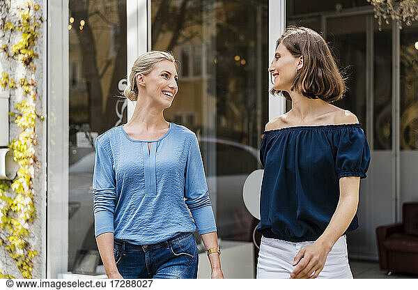 Lächelnde Geschäftsfrauen  die sich beim Gehen außerhalb des Büros ansehen
