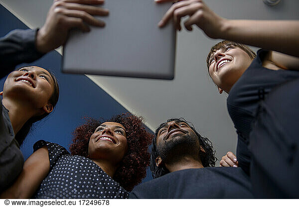 Lächelnde internationale männliche und weibliche Fachkräfte  die wegschauen und ein digitales Tablet im Büro halten