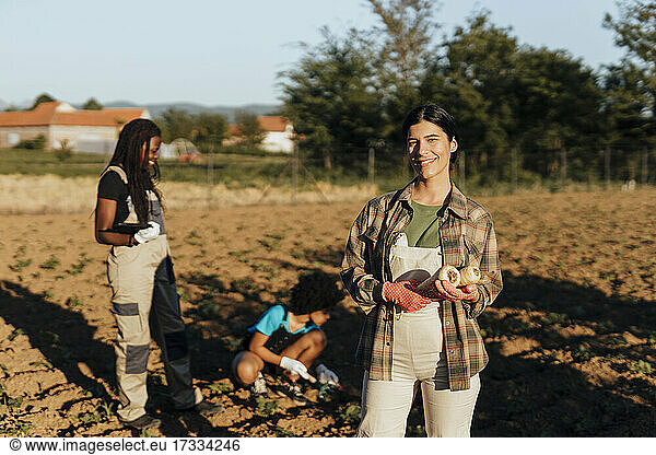 Lächelnde junge Bäuerin mit Radieschen auf einem Bio-Bauernhof an einem sonnigen Tag