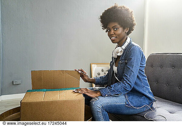 Lächelnde junge Frau beim Auspacken eines Pakets im heimischen Wohnzimmer