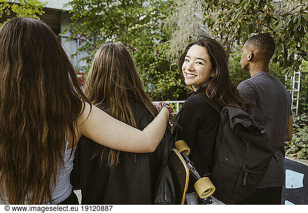 Lächelnde junge Frau  die beim Spaziergang mit Freunden in der Stadt zurückblickt