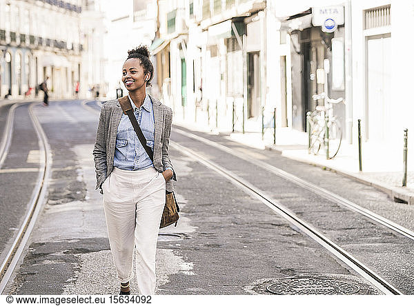 Lächelnde junge Frau mit drahtlosen Kopfhörern in der Stadt unterwegs  Lissabon  Portugal