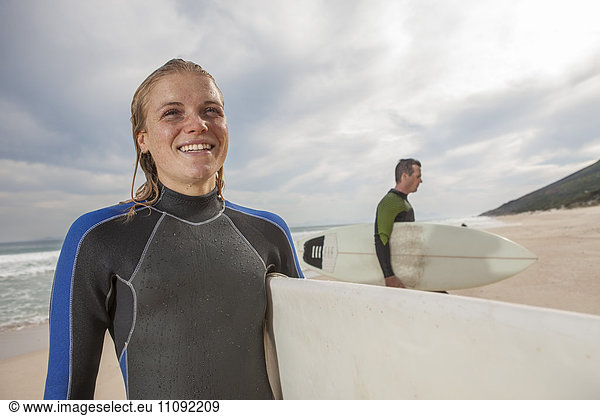 Lächelnde junge Frau mit Surfbrett am Strand