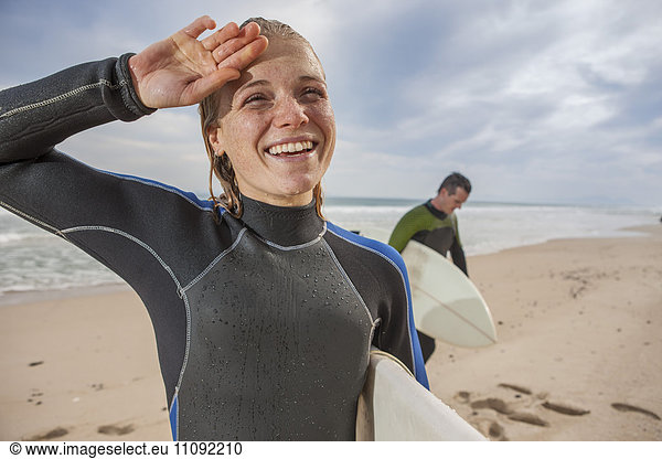 Lächelnde junge Frau mit Surfbrett am Strand