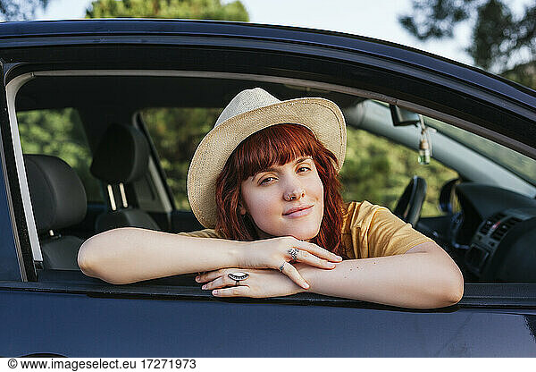 Lächelnde junge schöne rothaarige Frau  die sich aus dem Autofenster lehnt