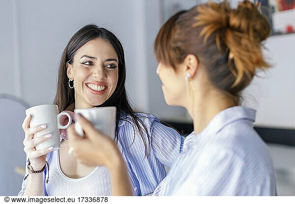 Lächelnde Kolleginnen  die sich beim Kaffeetrinken im Studio ansehen