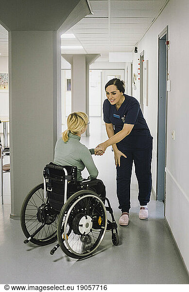 Lächelnde Krankenschwester  die einen im Rollstuhl sitzenden Patienten im Krankenhaus begrüßt