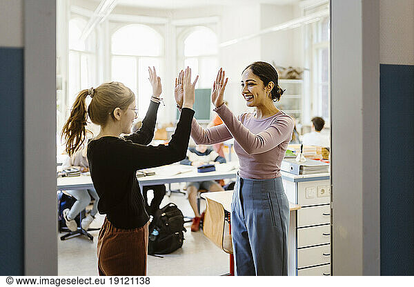 Lächelnde Lehrerin  die einem Mädchen im Klassenzimmer die Hand drückt