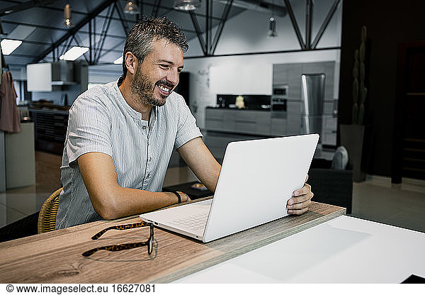 Lächelnde männliche Fachkraft  die auf einen Laptop schaut  während sie freiberufliche Arbeit im Büro erledigt