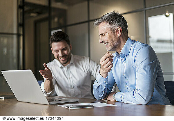 Lächelnde männliche Fachleute  die in einem Sitzungssaal über einen Laptop diskutieren